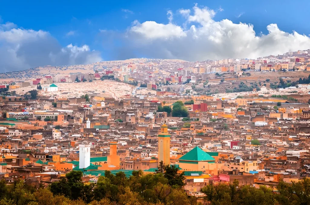 An aerial view of the Fes Medina, a highlight of Fes Morocco attractions, with narrow streets, ancient buildings, and green-domed mosques under a sunset, a top spot for things to do in Fes.