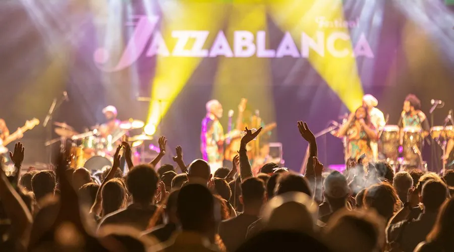A lively crowd with raised hands at the Jazzablanca Festival, a highlight when you visit Casablanca, cheering for musicians on stage under bright lights with the festival name “Jazzablanca” in the background, a top Casablanca attraction.