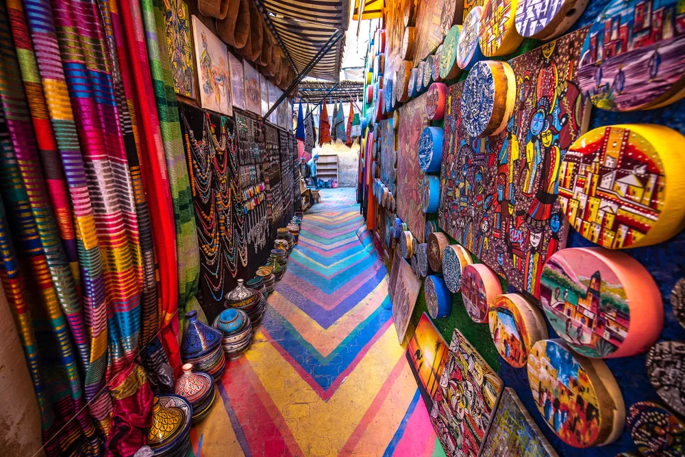 The vibrant souk in Fes, a top thing to do in Fes, with colorful textiles, hand-painted ceramics, and souvenirs along a rainbow-painted alley in the medina, a key Fes Morocco attraction.